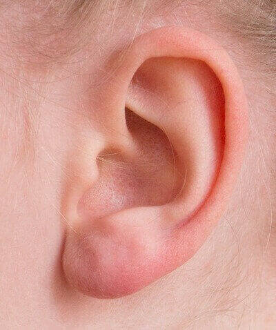 Close-up of a pink, human ear against light skin.