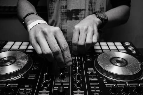 Two hands adjusting knobs on a black DJ controller with silver platters.