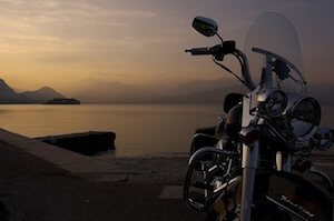 Black motorcycle with chrome details beside a calm lake at sunset.