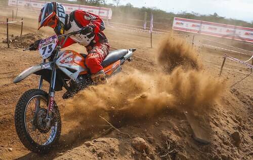A motocross rider in red and white gear kicks up dust on a dirt track.