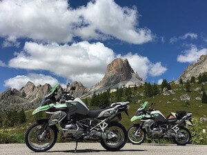 Two green and black motorcycles parked against a mountainous landscape and blue sky.