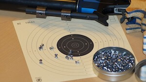 A black target sheet with silver pellets and a blue rifle on a wooden surface.