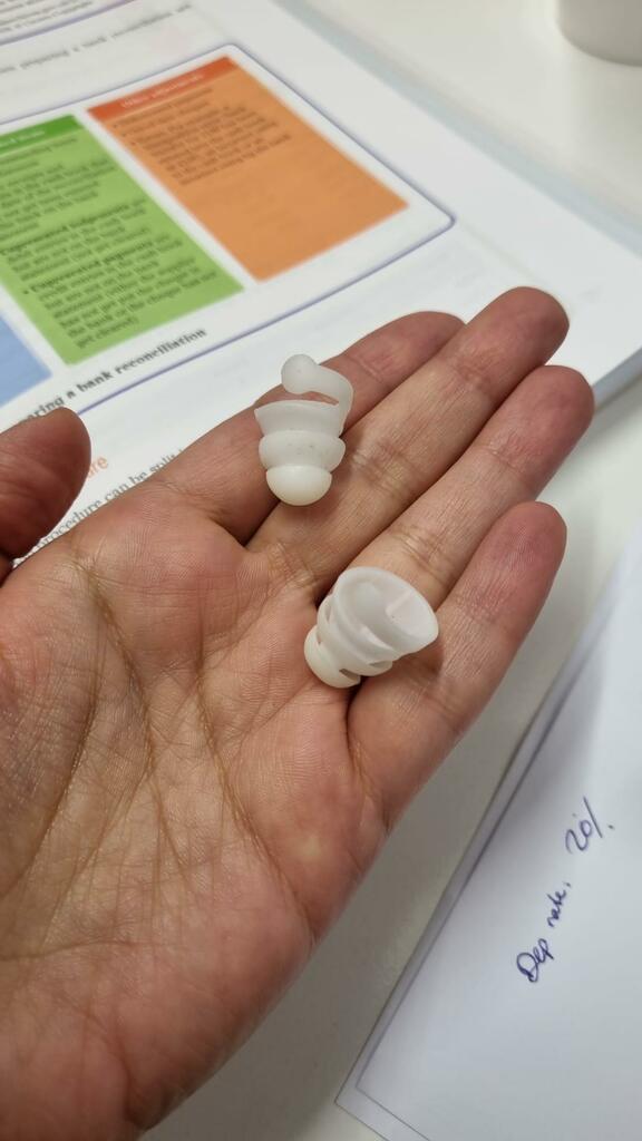 A hand holding two small white silicone earplugs over a document and notes.
