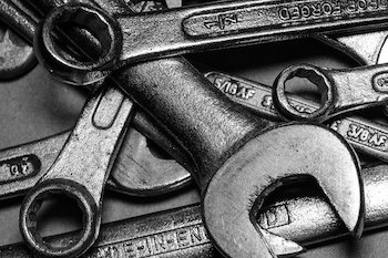 A pile of silver metal wrenches arranged haphazardly on a grey surface.