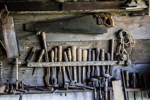 A wooden wall displaying various rusty tools, including saws, chisels, and hammers.
