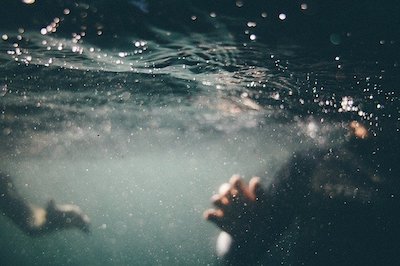 Underwater scene with blurred hands, shimmering water, and bubbles in shades of blue.