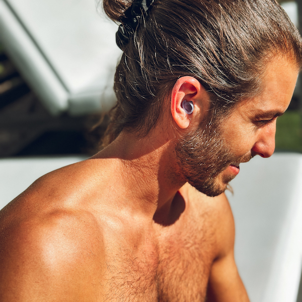 A man with long hair and a beard wearing wireless earphones, in sunlight.