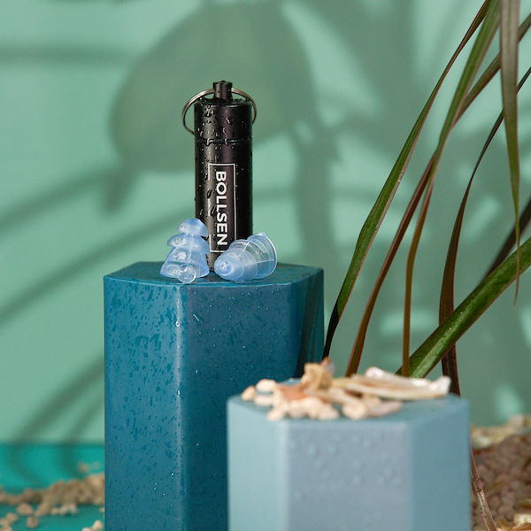 Black keychain flashlight, blue earplugs, and decorative shells on teal textured surfaces.