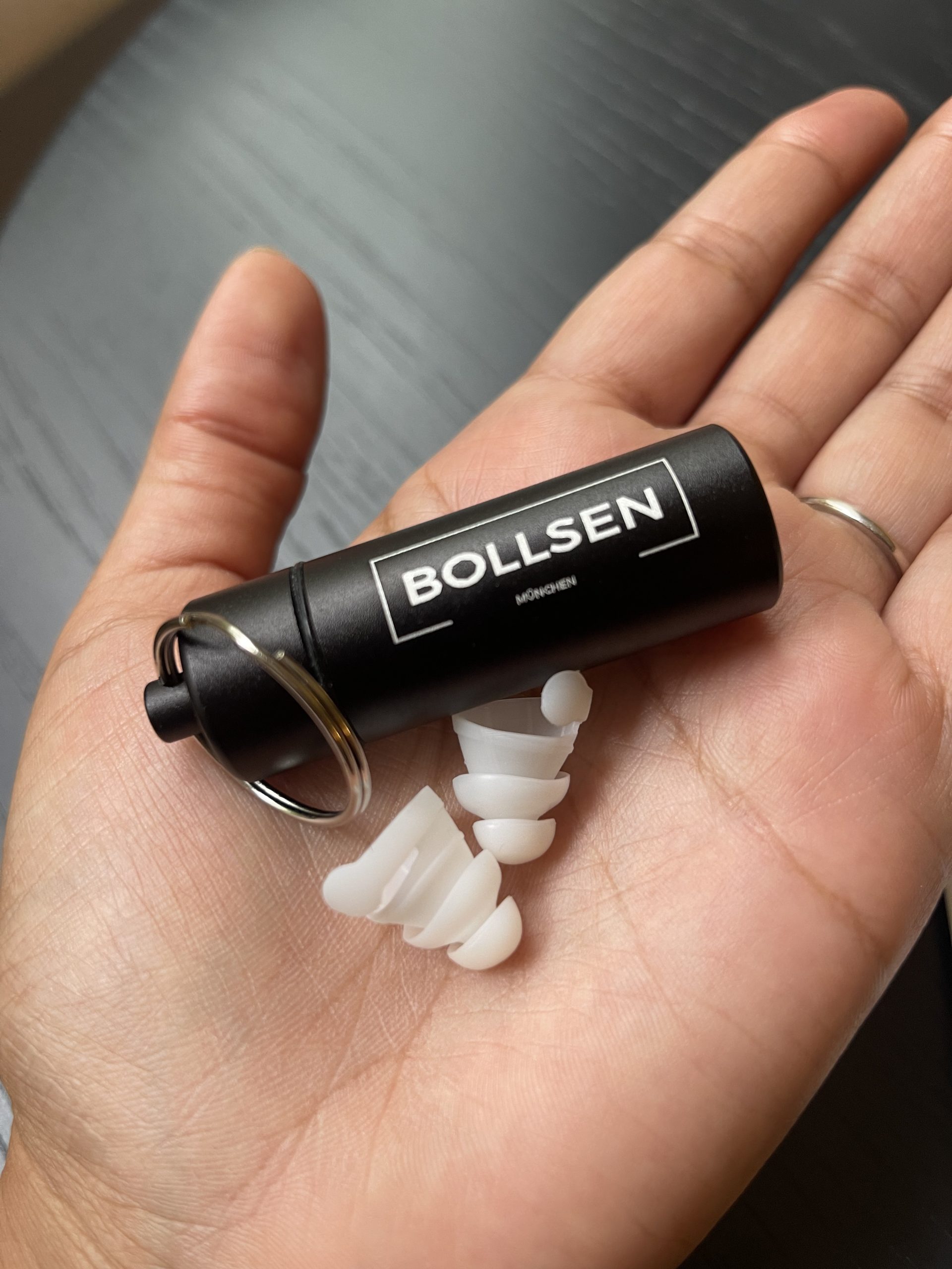 A black cylindrical case in a hand, with white earplugs beside it.