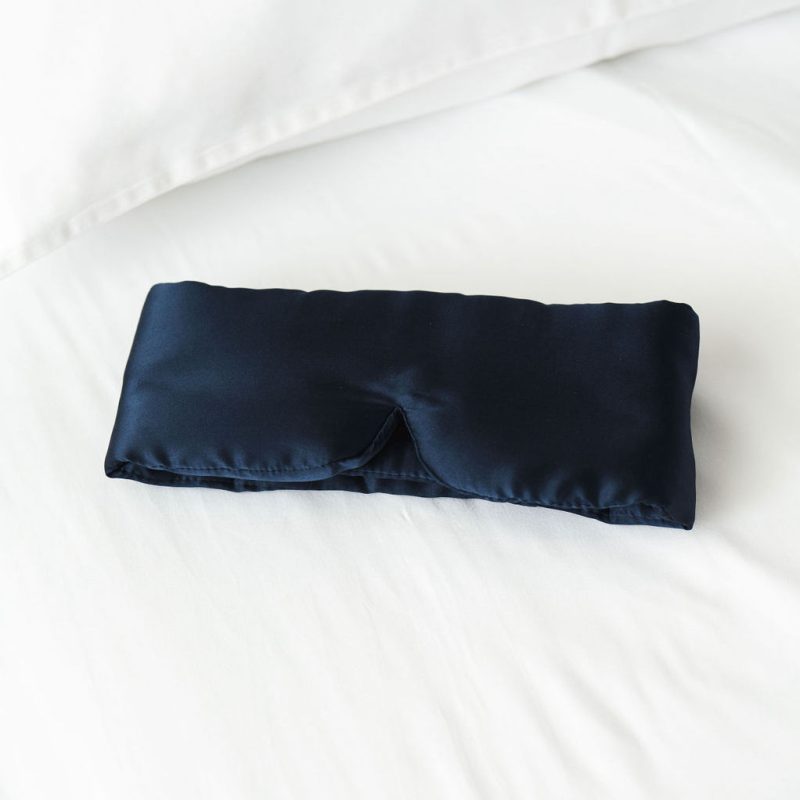 Navy satin sleep mask resting on a white bedspread.