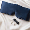 Navy eye mask, black tube, and white earplugs on cream fabric background.