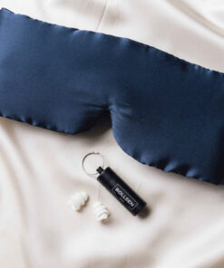 Navy eye mask, black tube, and white earplugs on cream fabric background.