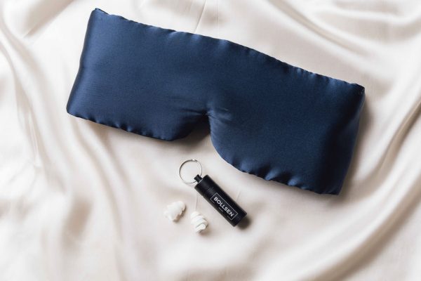Navy eye mask, black tube, and white earplugs on cream fabric background.