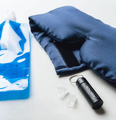 Blue water bottle, dark blue sleep mask, black keychain, and white earplugs on a surface.