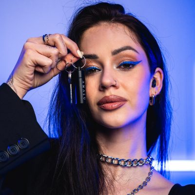 A woman with blue eyeliner holds black keychain in a stylish outfit.