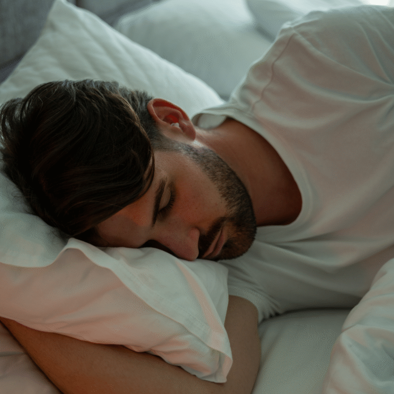 Man sleeping peacefully on white pillows, wearing BOLLSEN Earplugs Hearing Protection.