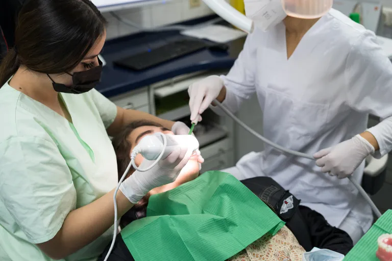 Dental clinician using an ultrasonic scaler and suction on a patient, one of the high-frequency noise sources at the chair
