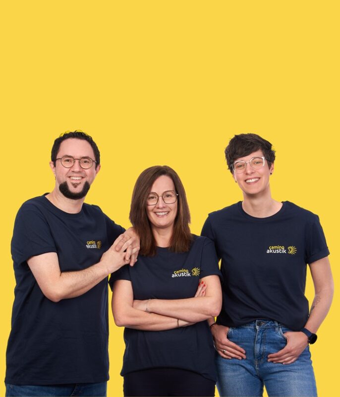 Hearing acousticians from Camino Akustik in Elsenfeld, Bavaria, in branded T-shirts against a yellow background